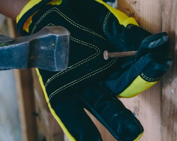 Worker using a hammer and nail on a wooden surface with protective gloves.